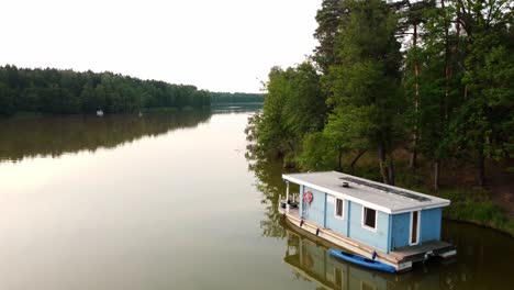 House-boat-floating-in-a-green-natural-lake-next-to-a-forest-in-Brandenburg,-Germany