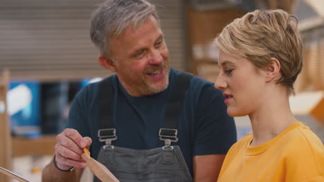 close up of female apprentice learning skills from mature male carpenter in furniture workshop