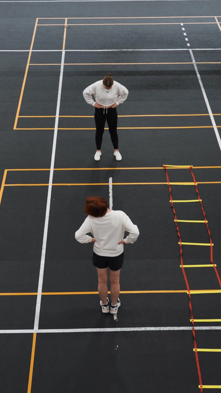 Instructor blanco guiando ejercicios rápidos de juego de pies, repeticiones dinámicas con escalera de agilidad, pasos de sprint, señales de tiempo, indicaciones del entrenador, sudor y concentración en las marcas de la cancha urbana, ritmo enérgico