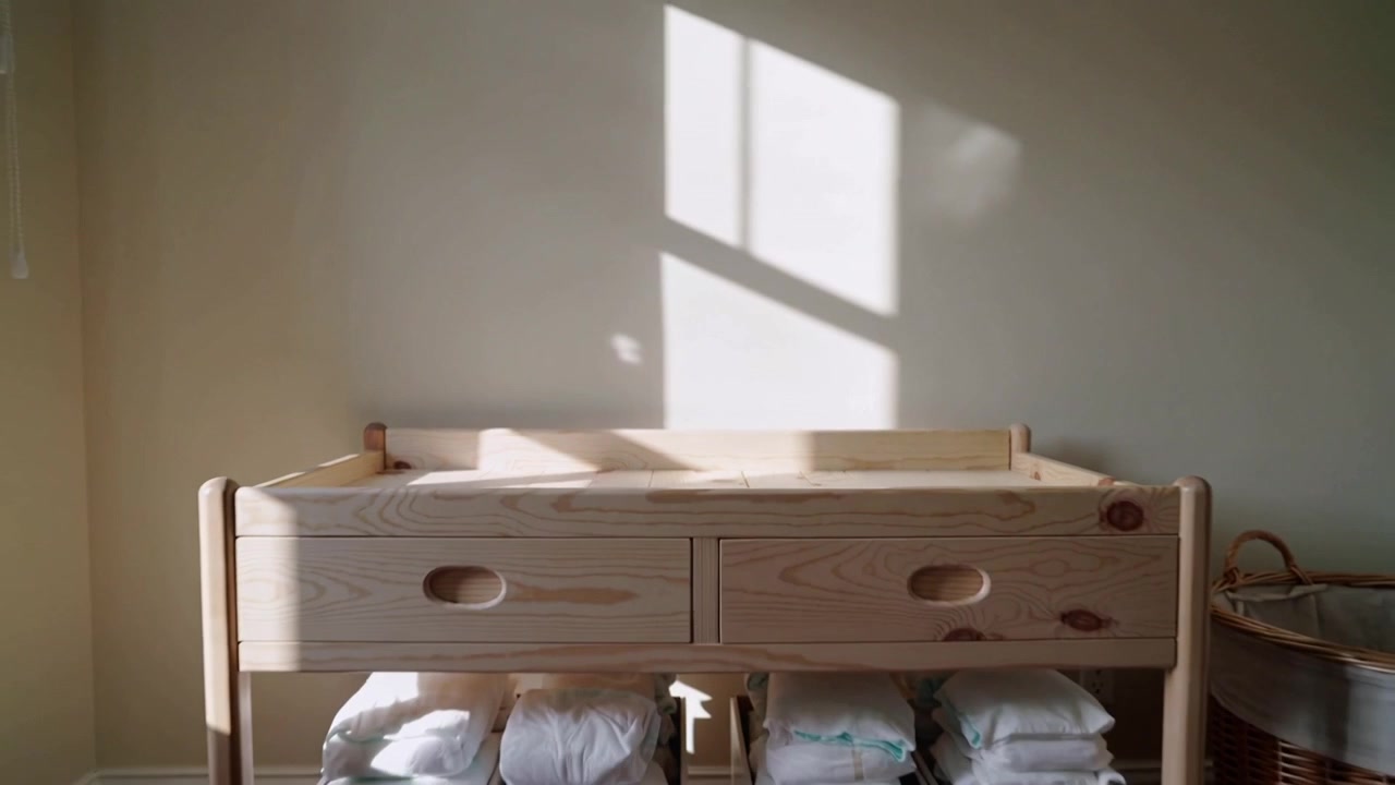 Camera pulling back, pine changing table staying still by window in nursery, revealing diaper bins