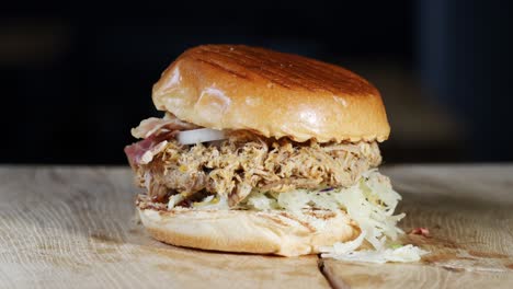 a burger with bread, barbecue sauce, coleslaw, pulled meat, onion rings and bacon is presented rotating