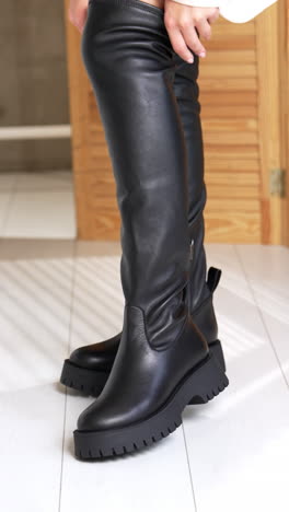 female wearing the high black boots and pulling them by the shaft. elegant stylish footwear demonstration in studio. vertical video