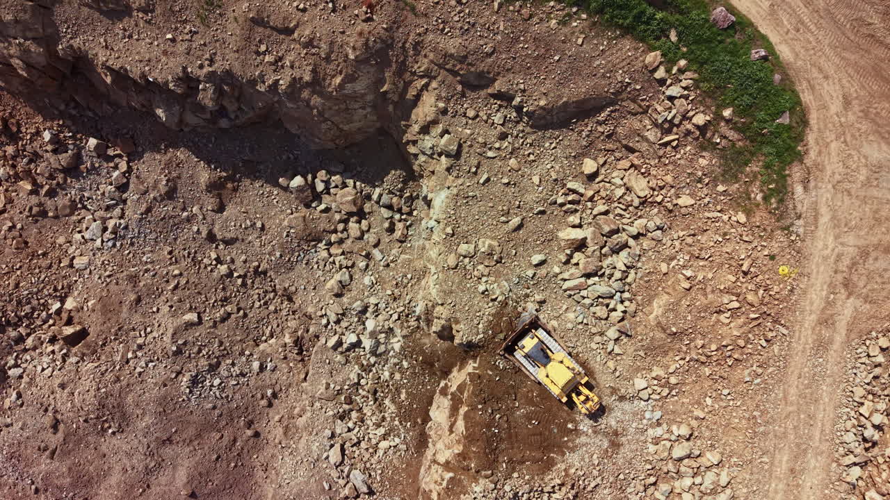 Un veicolo da scavo lavora su terreno roccioso in un cantiere durante una giornata di sole in un'area aperta.