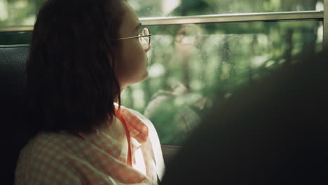school girl sitting bus alone close up. teen brunette looking window on greenery