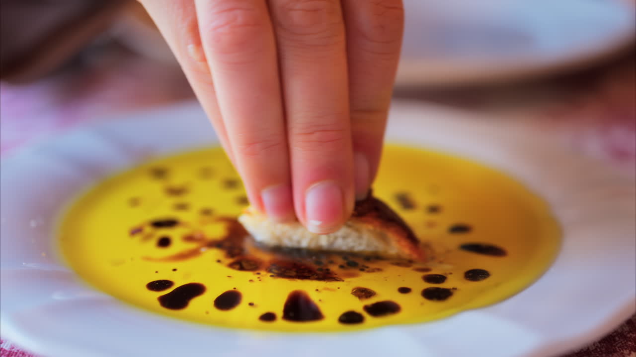 Close up of a woman dipping bread in olive oil with balsamic glaze drops and eating it at a restaurant