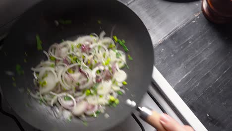 person shaking pan with spring onions with white onions