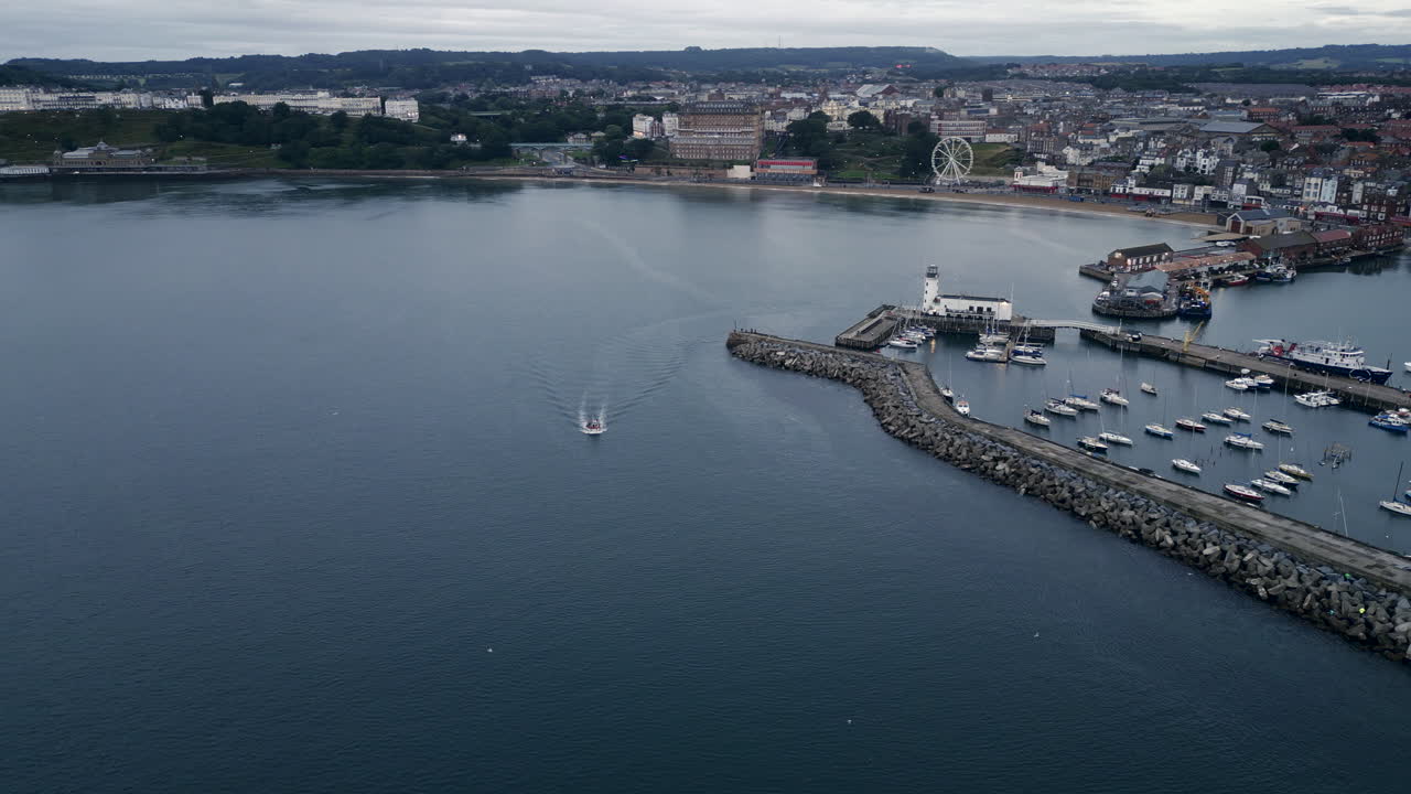 estableciendo un drone filmado sobre la bahía y el puerto de scarborough con un barco que sale en un día nublado