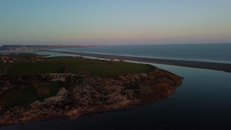 aerial footage over fields next to chisel beach in dorset at sunset. the drone moves forward while slowly turns left revealing portland beach road leading to portland island off the south coast.