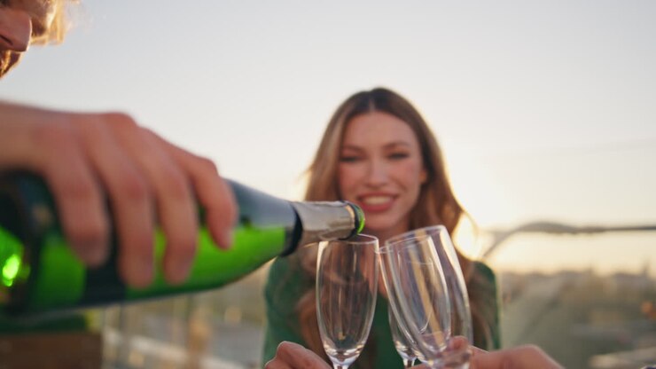Primo piano di persone che versano champagne in calici di vetro a un raduno sul tetto.