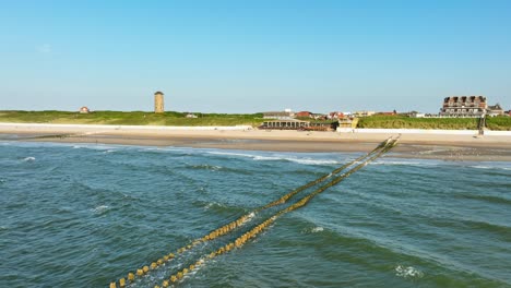 aerial shot flying over the surf towards a beach tent outside a picturesque little coastal town on a cloudless summer evening