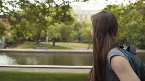 female student casually and curiously walking through campus exploring near water, side profile shot