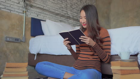 Asian-student-surrounded-with-books-sitting-on-the-floor-with-her-legs-crossed-and-preparing-for-exams