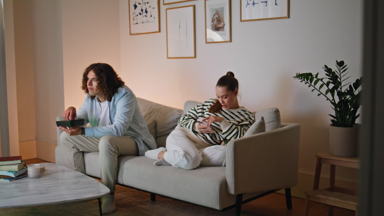 Spouses spending weekend evening in apartment sitting separately on cozy couch
