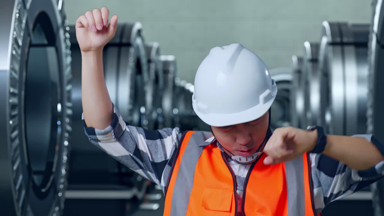 안전 헬을 착용한 아시아 남성 엔지니어가 골을 외치며 금속 공장에서 춤을 추며 축하합니다.