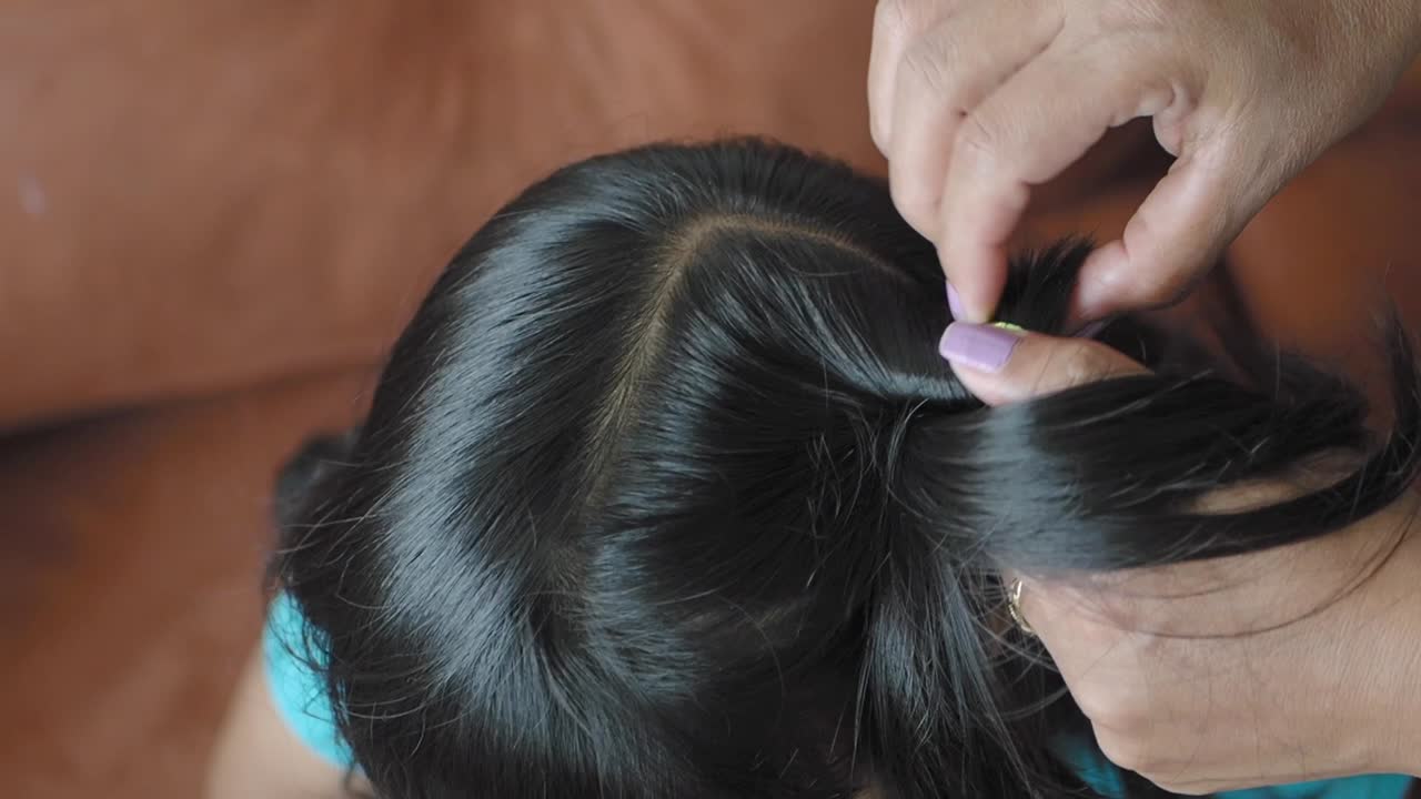 작은 소녀가 그녀의 머리카락을 귀여운 포니테일로 스타일링하고 있습니다.