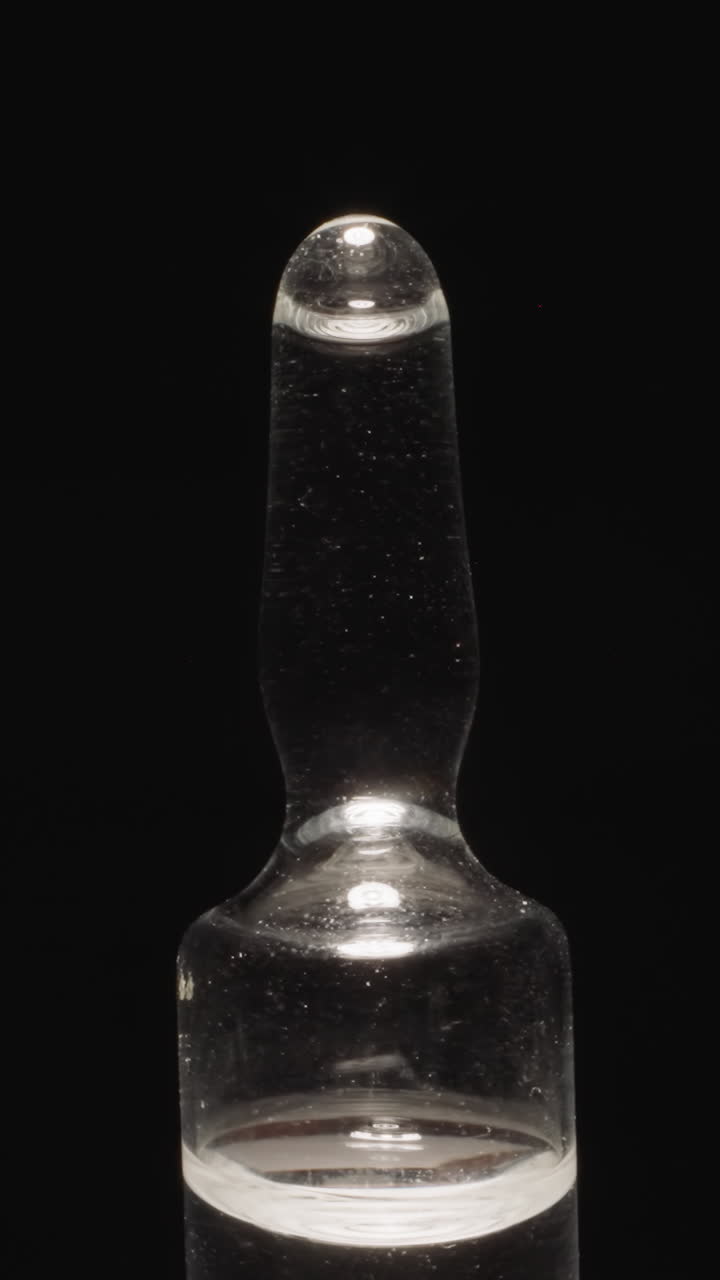Sealed glass ampoule with long tip on black background. Empty capsule designed for liquids for injections reflecting bright studio light macro