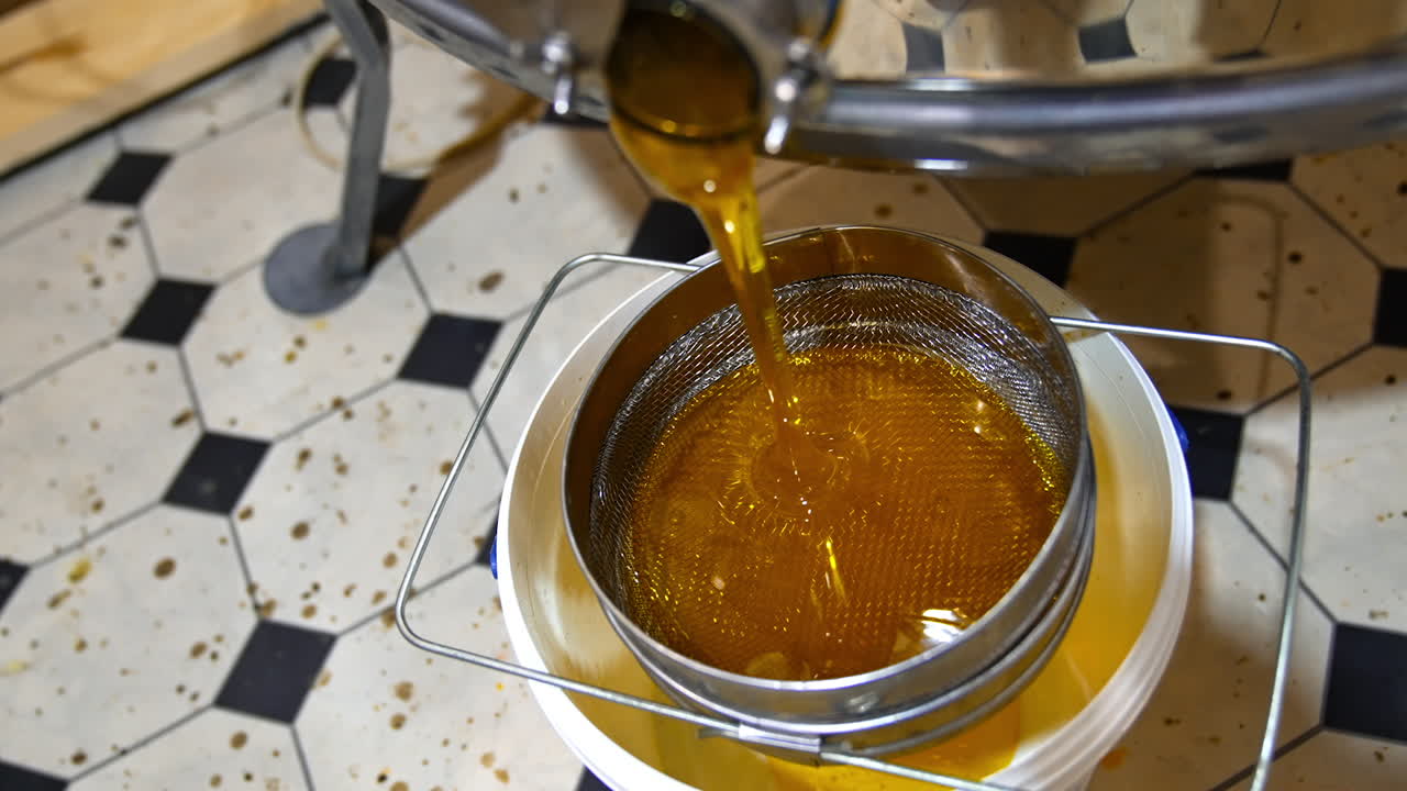 Fresh honey leaking from the faucet of honey extracting machine after pumping. Liquid organic product flowing on the sieve. Top view.