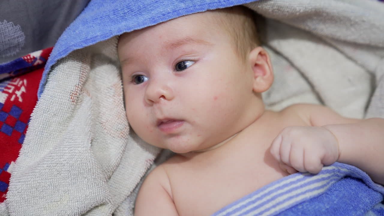 Cute baby lying covered with towel. Mother is playing with her kid, holding his little fist. Close up.