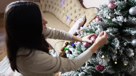 pregnant woman add decorations on green indoor artificial christmas tree