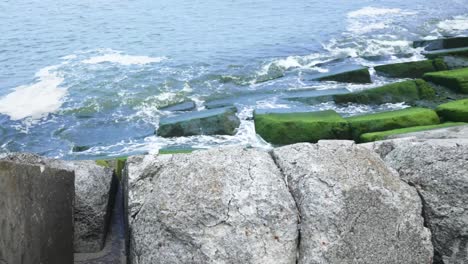 Sea-waves-crashing-on-mossy-wave-breaker-rocks,-pan-shot