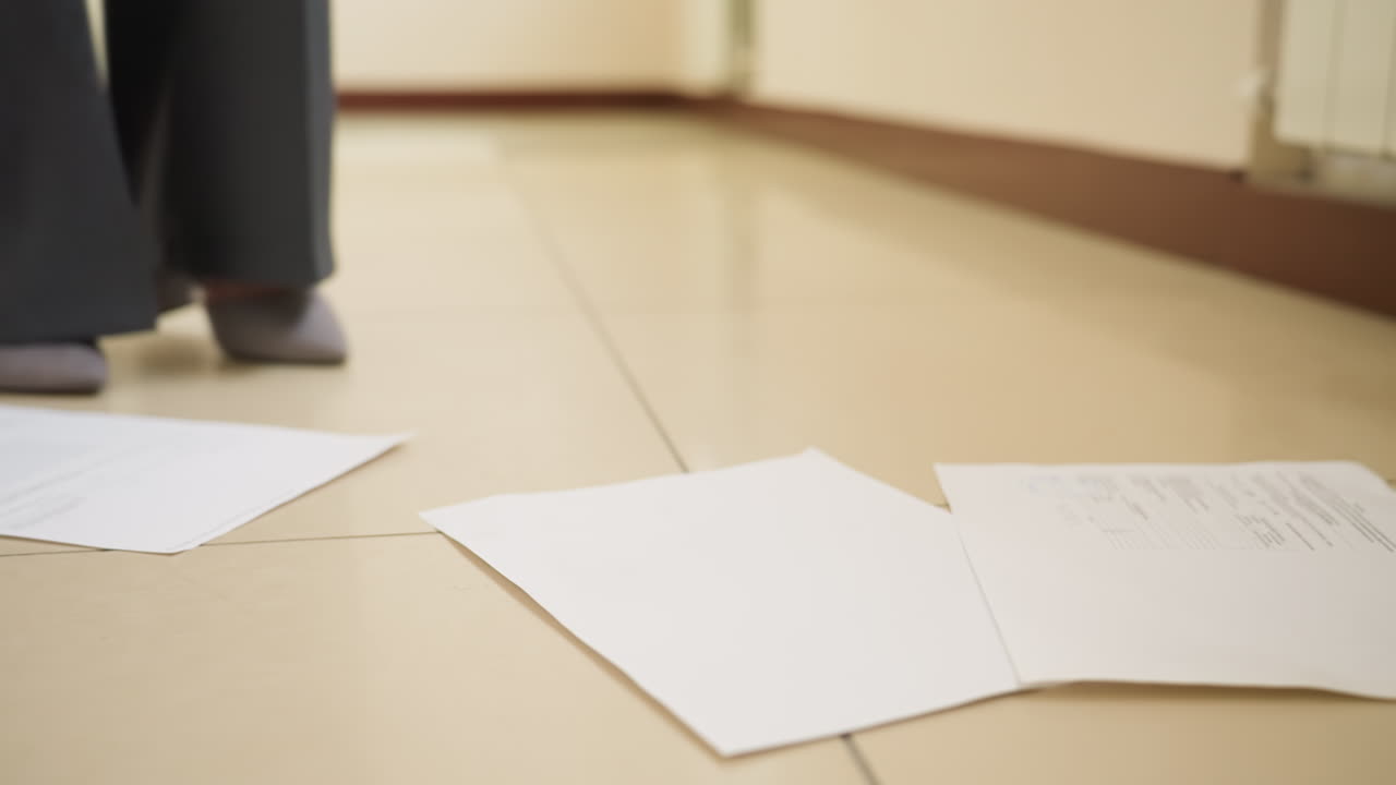 Scattered documents lie on tiled floor near businesswoman s feet in hallway, suggesting papers were accidentally dropped during walk, conveying urgency, workplace stress, or unexpected interruption