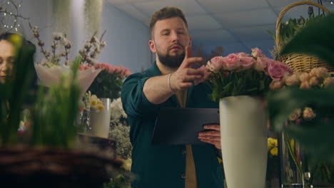 male florist counts flowers in vase and takes order using tablet