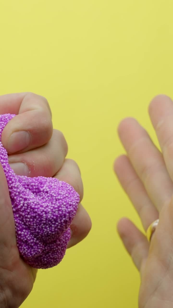 Fingers squishing pink foam slime on bright yellow background, vertical