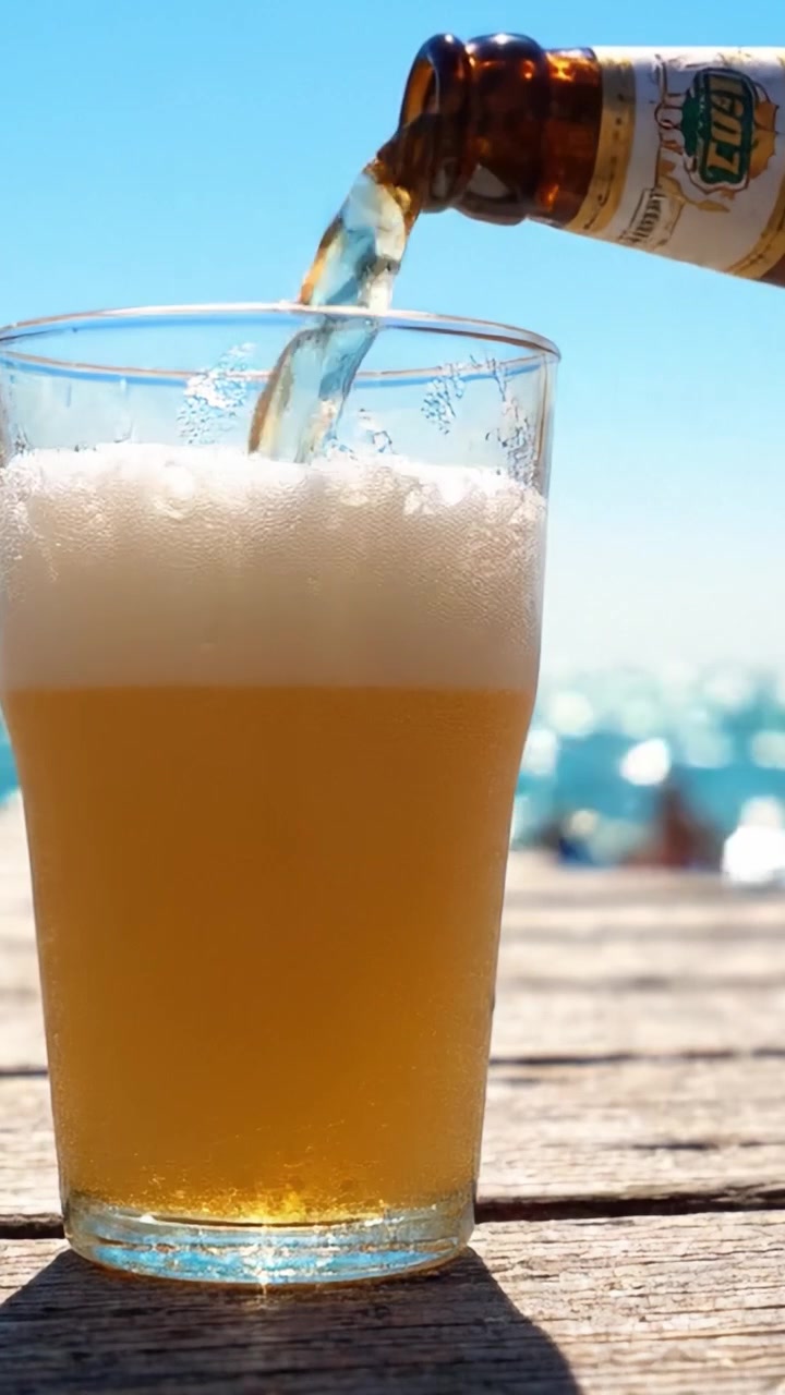 Una deliziosa bevanda rinfrescante: birra fredda versata in un bicchiere con lo sfondo panoramico di un oceano blu, bollicine e schiuma