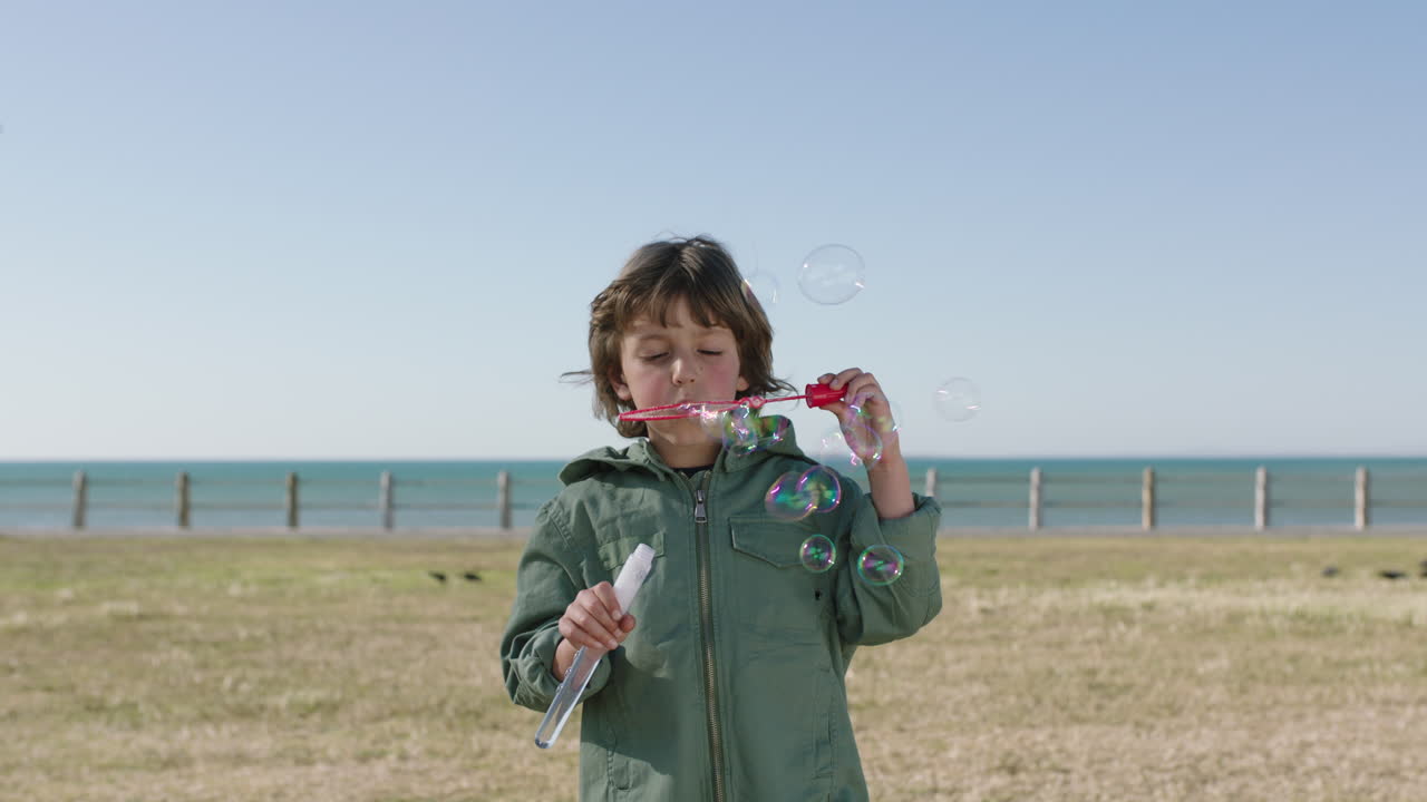 retrato de un lindo niño caucásico soplando burbujas disfrutando de un día feliz en la playa costera