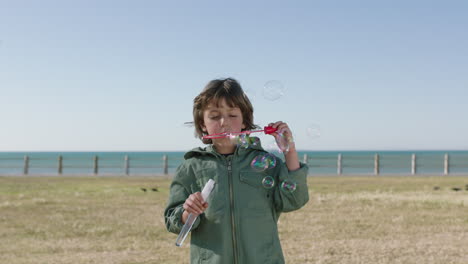 portrait of cute caucasian boy blowing bubbles enjoying happy day on seaside beach