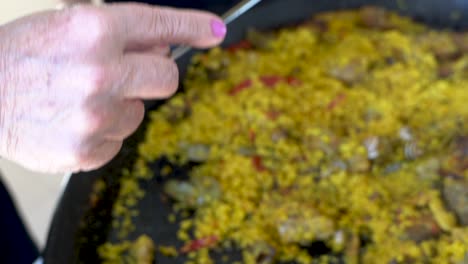 A-top-down-shot-of-a-hand-carrying-a-metal-ladle-scoops-up-the-fluorescent-yellow-Spanish-Paella-and-puts-it-onto-a-plate-that-is-out-of-the-shot,-Slow-motion-close-up