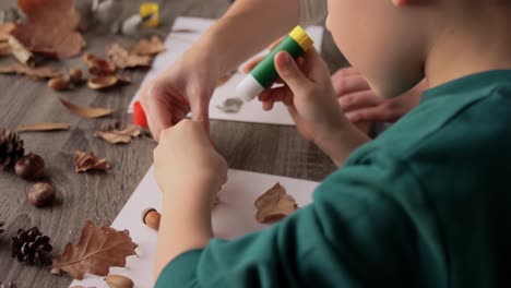 Mutter-Und-Sohn-Machen-Bilder-Von-Herbstblättern.Familien-,-Kreativitäts--Und-Bastelkonzept-–-Mutter-Und-Kleiner-Sohn-Machen-Mit-Klebestiften-Und-Papier-Zu-Hause-Bilder-Von-Trockenen-Herbstblättern,-Tannenzapfen-Und-Kastanien