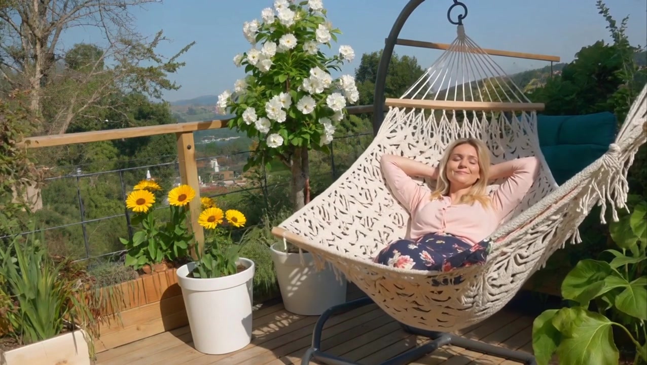 Entspannte Frau in Hängematte auf sonnigem Balkon
