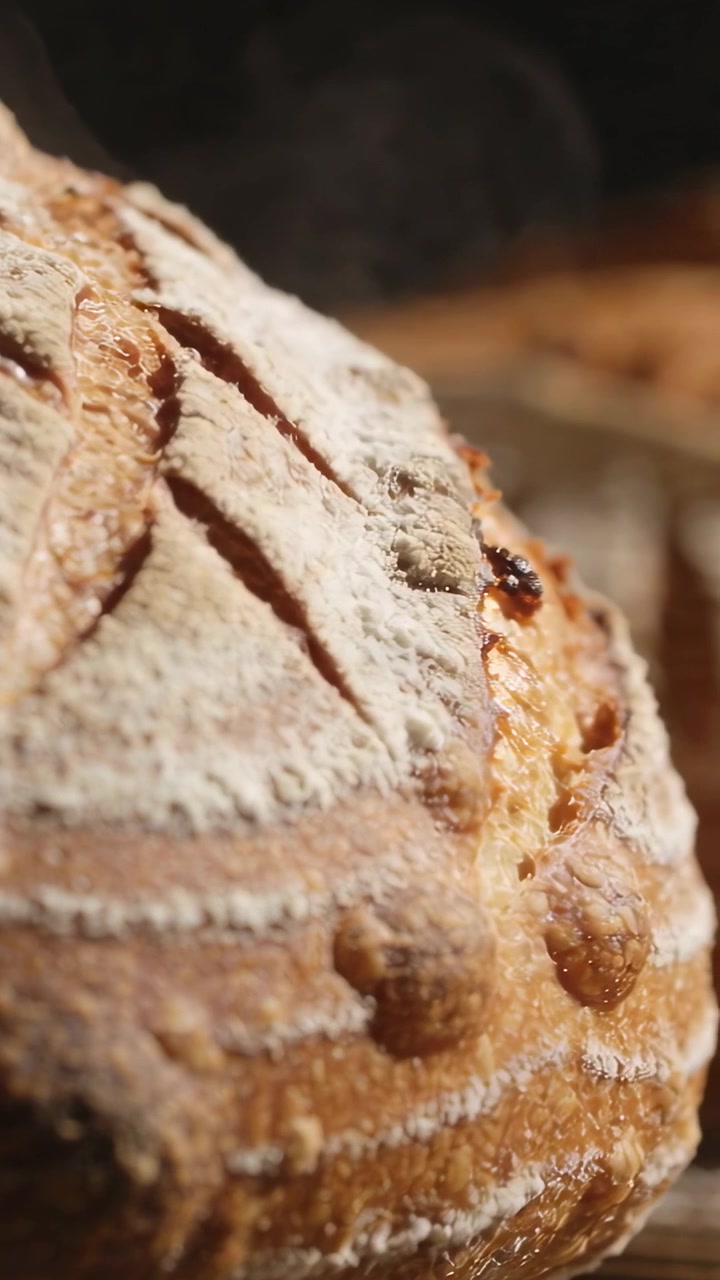 Vertical video: Releasing steam fresh from oven, artisan loaf cooling on rack, showing scored crust