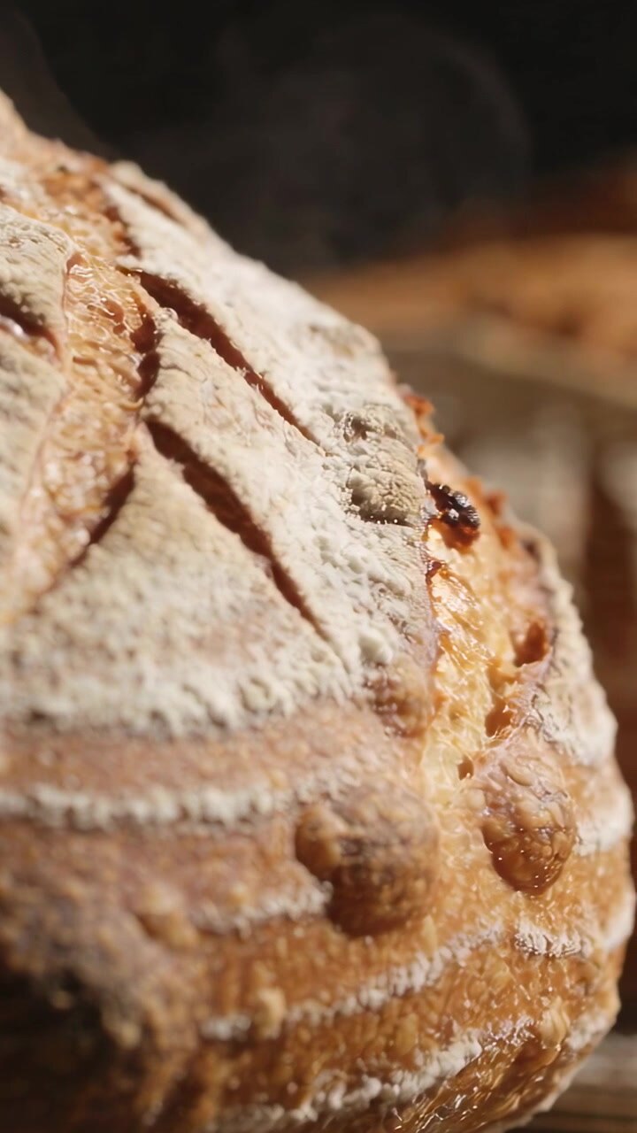 Vertical video: Releasing steam fresh from oven, artisan loaf cooling on rack, showing scored crust