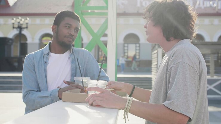 Male Friends Chatting While Sharing Pizza And Drinking, Standing At An Outdoor Table In The Street