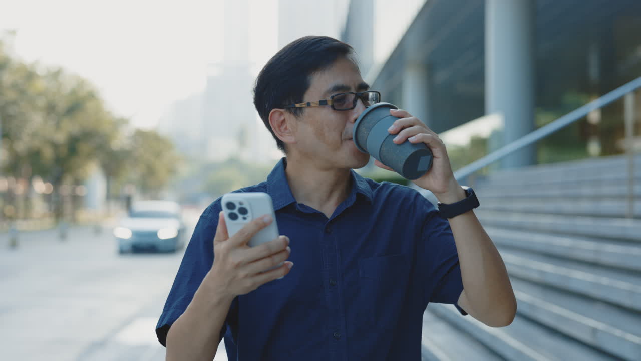 Man walking and using smartphone while drinking coffee in the city