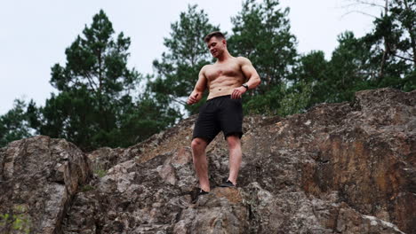 caucasian strongman stands on the high rock. sportsman with naked torso demonstrating his athletic body. low angle view.