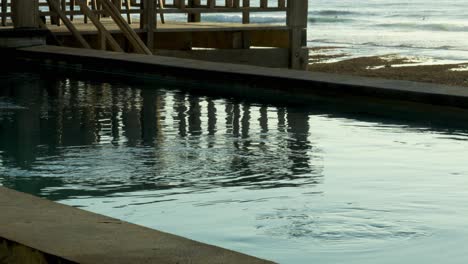 static shot of an infinity pool with water in the wind overlooking suluban beach during ebb tide in front of the beautiful sunset