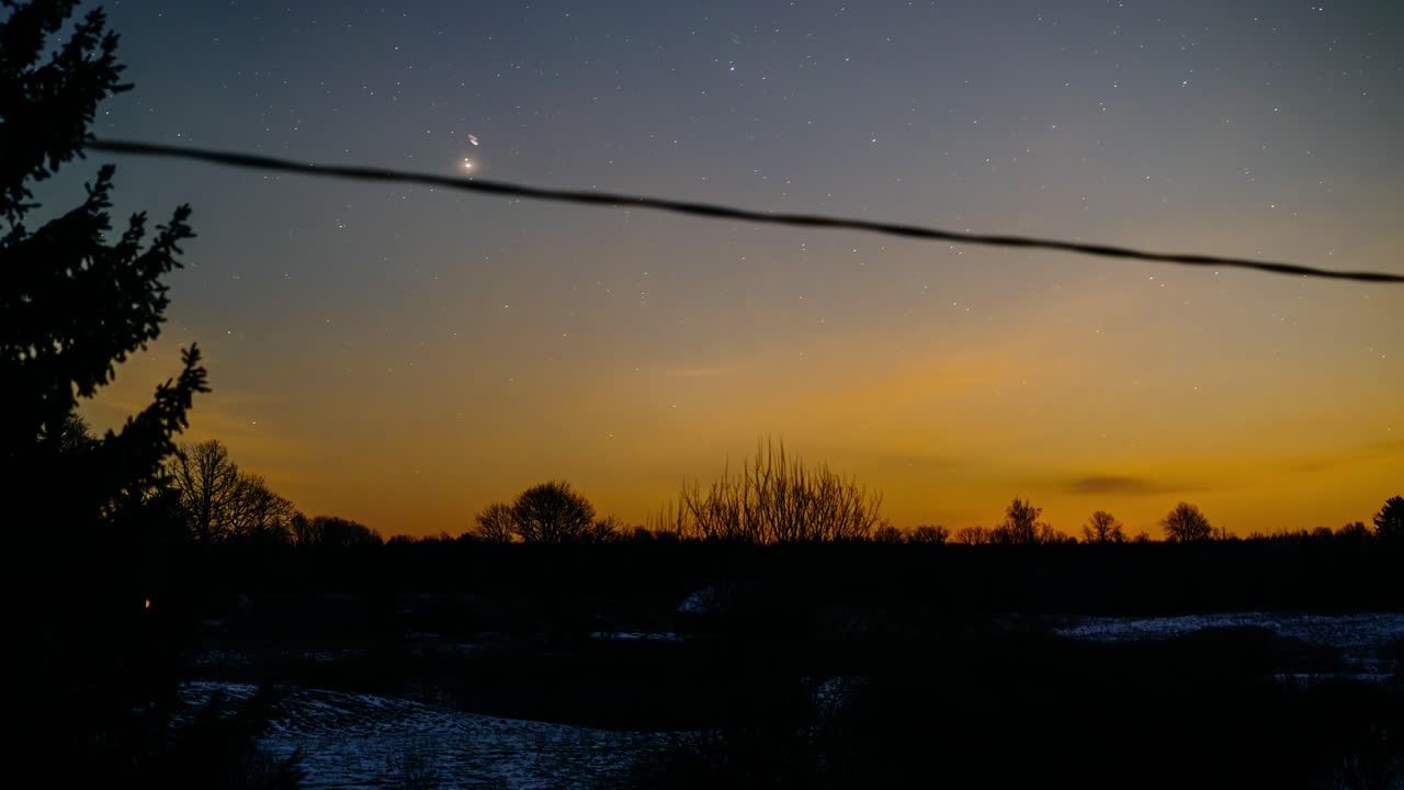 Moonlit skies over the countryside landscape at night with stars and light pollution from a city far away.