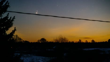 moonlit skies over the countryside landscape at night with stars and light pollution from a city far away.