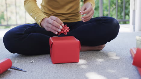 Midsection-of-biracial-woman-sitting-on-floor-packing-christmas-presents,-slow-motion