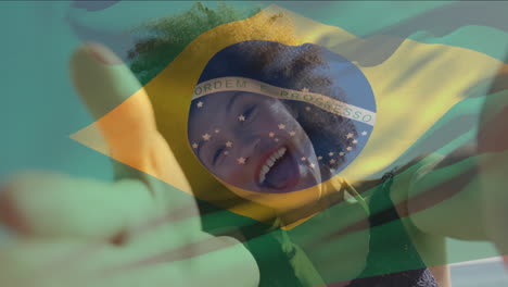 animation of flag of brazil waving over biracial woman talking selfie video with camera at beach