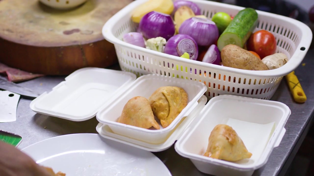 Tangkapan jarak dekat tangan meletakkan samosa keemasan ke dalam kotak kemasan putih dekat sayuran segar