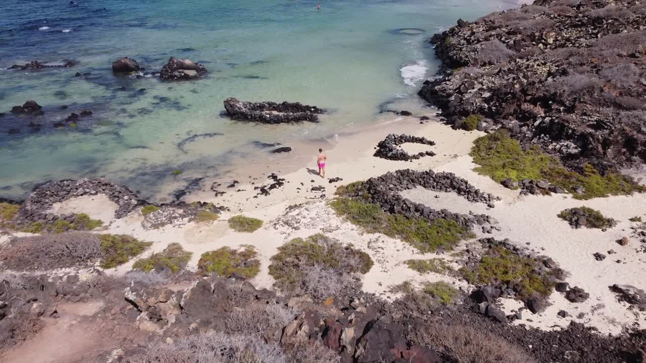 imágenes aéreas de drones de un chico relajándose en una bonita playa con aguas turquesas en lanzarote, islas canarias