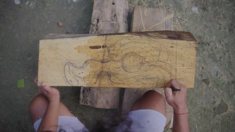 person sketching on wood with pencil the shape of a mask to carve