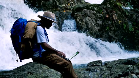 young man using green screen laptop computer on a waterfall. travel and freelance work concept