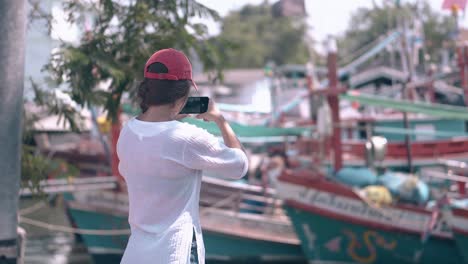 una turista dispara una bahía pictórica con barcos en un teléfono móvil.