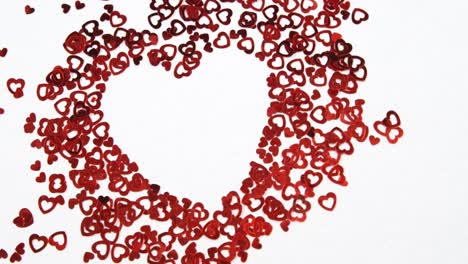 confeti de corazones rojos formando un corazón en una superficie blanca 4k