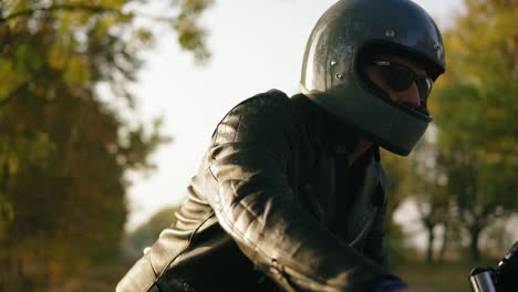 Un-Joven-Con-Chaqueta-De-Cuero-Negro-Y-Casco-Con-Gafas-De-Sol-Mientras-Está-Sentado-En-Su-Motocicleta-Preparándose-Para-Comenzar-Su-Viaje